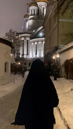 a woman walking down a snow covered street in front of a large white building with gold domes