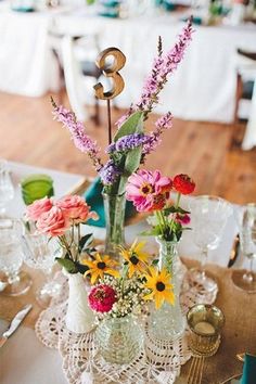 an arrangement of flowers in vases on a table with place settings and napkins