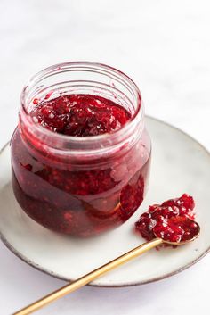 a jar of raspberry jam on a plate with a spoon