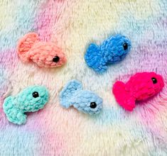 four small crocheted fish are laying on a colorful blanket, one is blue and the other is pink