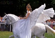 a woman riding on the back of a white horse next to an angel wings costume