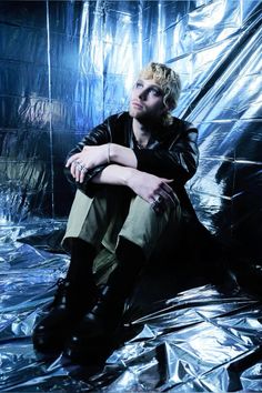 a young man sitting on top of a shiny sheet covered floor with his legs crossed