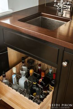 a kitchen sink with an open drawer in the middle that holds liquor bottles and other condiments