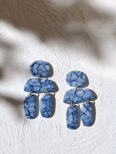 two pairs of blue and white marble earrings on a white surface with shadow from the sun