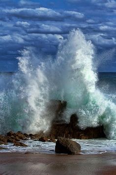 an ocean wave crashing on rocks in front of the ocean