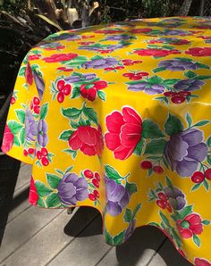 a yellow table cloth with colorful flowers on it sitting on a wooden deck next to trees