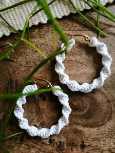 two white crocheted hoop earrings sitting on top of a piece of wood next to green grass