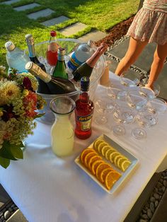 a table topped with bottles and glasses filled with alcohol next to flowers on top of a grass covered field