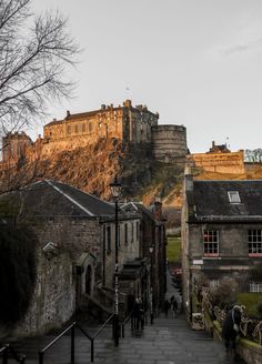 an old castle on top of a hill with people walking up the stairs to it