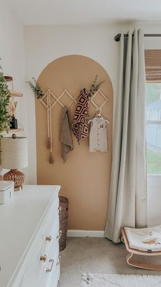 a baby's room with a crib and hanging clothes on the wall next to a window