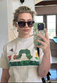 a woman taking a selfie in front of a mirror with her cell phone and the very hungry caterpillar t - shirt