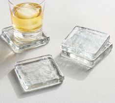 three square glass coasters with ice cubes on the bottom and one filled with liquid