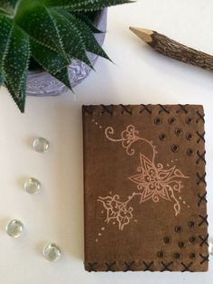 a brown notebook sitting on top of a white table next to a plant and pencil