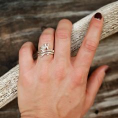 a woman's hand with a ring on it and a piece of driftwood in the background