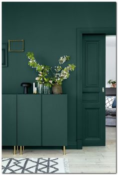 a living room with green walls and plants on the sideboard next to an open door