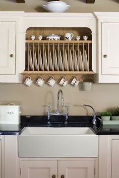 a white kitchen sink sitting under a wooden shelf filled with cups and saucer holders