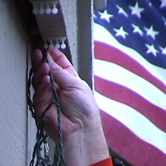 a hand is holding some barbed wire to the side of a building with an american flag in the background