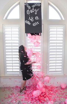 a woman standing in front of a window surrounded by pink balloons and confetti