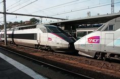 two white trains sitting on the tracks next to each other in front of a train station