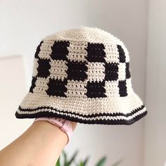 a crocheted hat with black and white squares on the brim is held up by a woman's hand