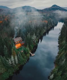 an aerial view of a cabin in the middle of a lake surrounded by trees and fog