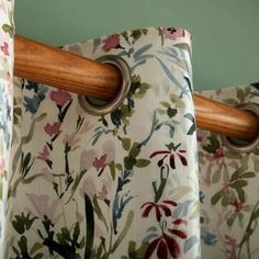 two curtains with wooden handles hanging from the curtain rod in front of floral print fabric