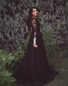 a woman wearing a black dress standing in front of bushes