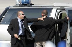 two men in suits and ties standing next to an suv with their hands on the door