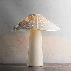 a white table lamp sitting on top of a wooden floor next to a gray wall