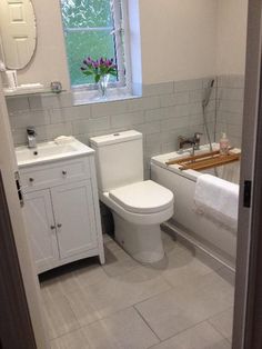 a white toilet sitting next to a bath tub in a bathroom with tile floors and walls