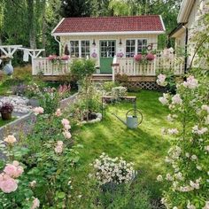 a small white house surrounded by flowers and greenery