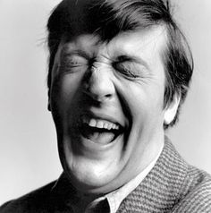 a black and white photo of a man laughing with his eyes wide open to the side