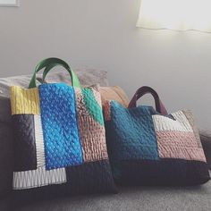 three colorful bags sitting on top of a couch next to each other in front of a window