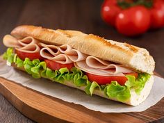 a sub sandwich with meat, lettuce and tomatoes on a wooden cutting board