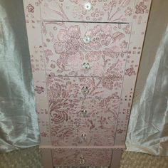 a pink and white dresser with ornate designs on the front, drawers and knobs