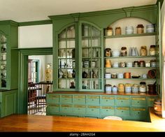 an old fashioned kitchen with green cupboards and shelves filled with jars, pans and utensils