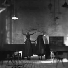 black and white photograph of two people standing in front of a table with chairs on it