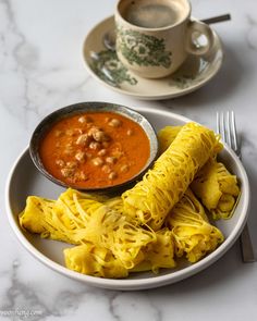 a white plate topped with pasta and sauce next to a cup of coffee on top of a table