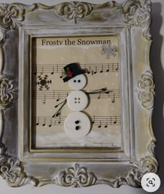 a snowman made out of buttons in a frame with music notes on the wall behind it