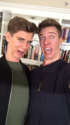 two men standing next to each other in front of a book shelf