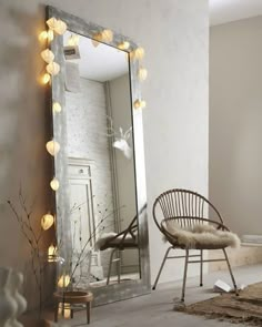 a white chair sitting in front of a large mirror with lights on the wall behind it