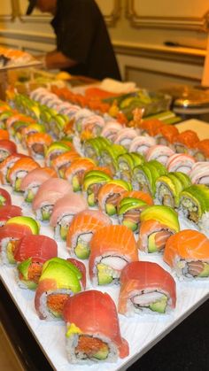 many sushi rolls are lined up on a long white platter with a man in the background