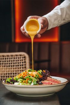 a person pouring sauce over a salad on top of a white plate with lettuce and carrots