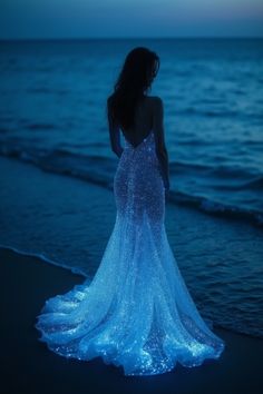 Elevate your bridal photography experience with this concept: a midnight-blue dress shimmering with a glow-in-the-dark, diamond-like brilliance.   This enchanting seaside setting invites the bride to embrace her own ethereal beauty, as if in the presence of mythical mermaids in the distance. Capture the magic of this moment, where the lines between reality and dreams blur, creating an unforgettable bridal portrait that celebrates the bride's ethereal allure. Dark Blue Dresses Aesthetic, Glow In The Dark Wedding Dress, Blue Mermaid Wedding Dress, Fancy Dress Photoshoot, Mythical Dresses, Dark Blue Wedding Dress, Ocean Themed Dress, Glow In The Dark Dress, Ocean Blue Dress