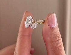 a woman's hand holding an engagement ring with two diamonds on top of it