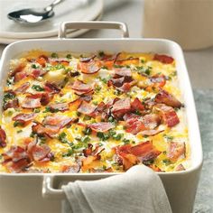 a casserole dish with bacon and cheese in it on a table next to silverware