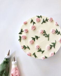 a cake decorated with pink roses and green leaves on top of a white table next to a pair of scissors