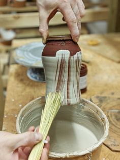 a person is painting a vase with white and brown stripes on the outside of it