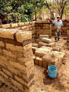 a man standing next to a pile of bricks on top of a dirt field with a bucket