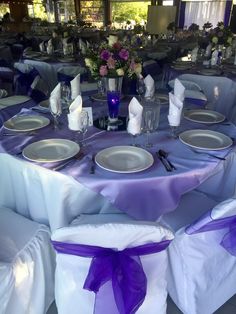 the table is set with purple and white linens, silver plates and napkins